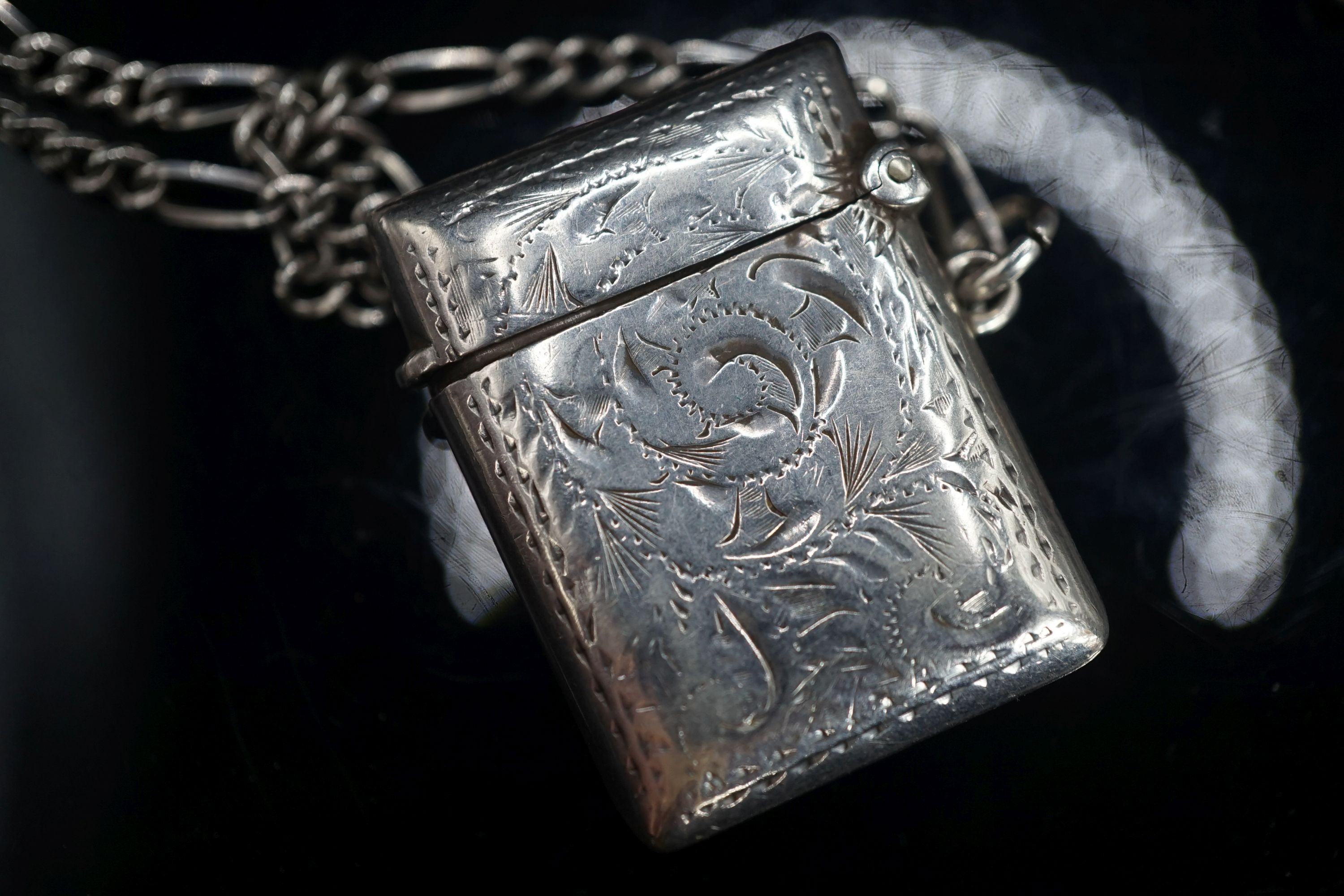 A modern silver pendant necklace, a silver vest case and a sterling chain.